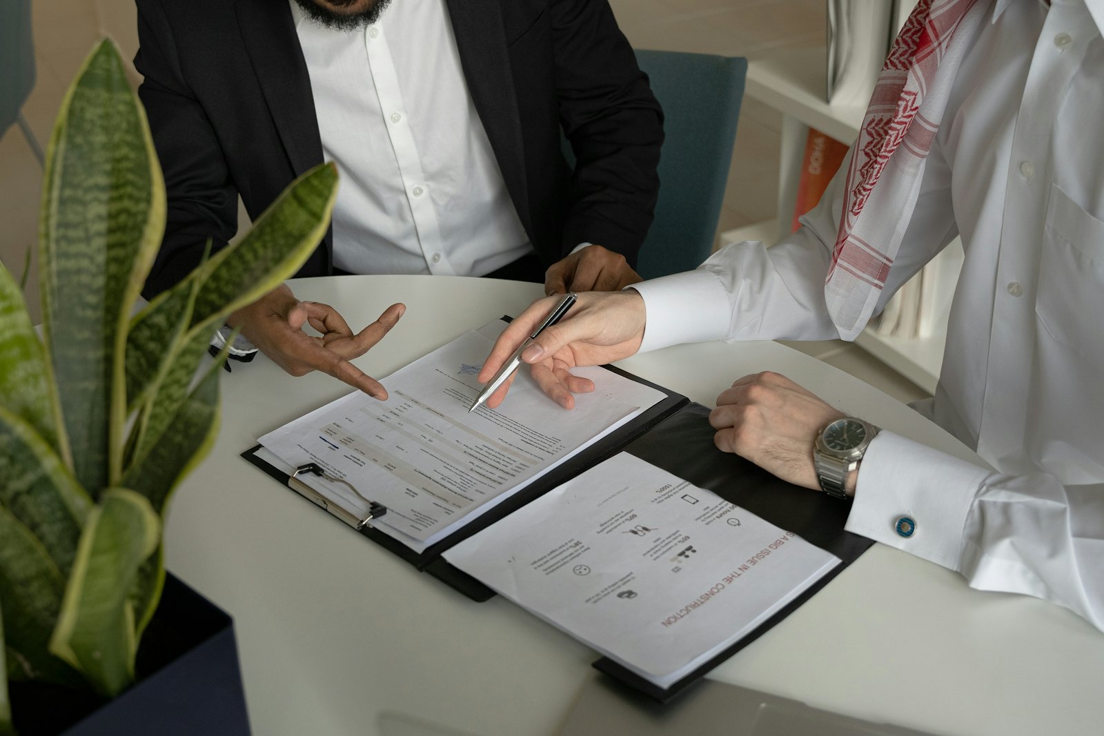 Deux professionnels assis à une table reprennent ensemble un contrat imprimé, stylo posé sur les pages