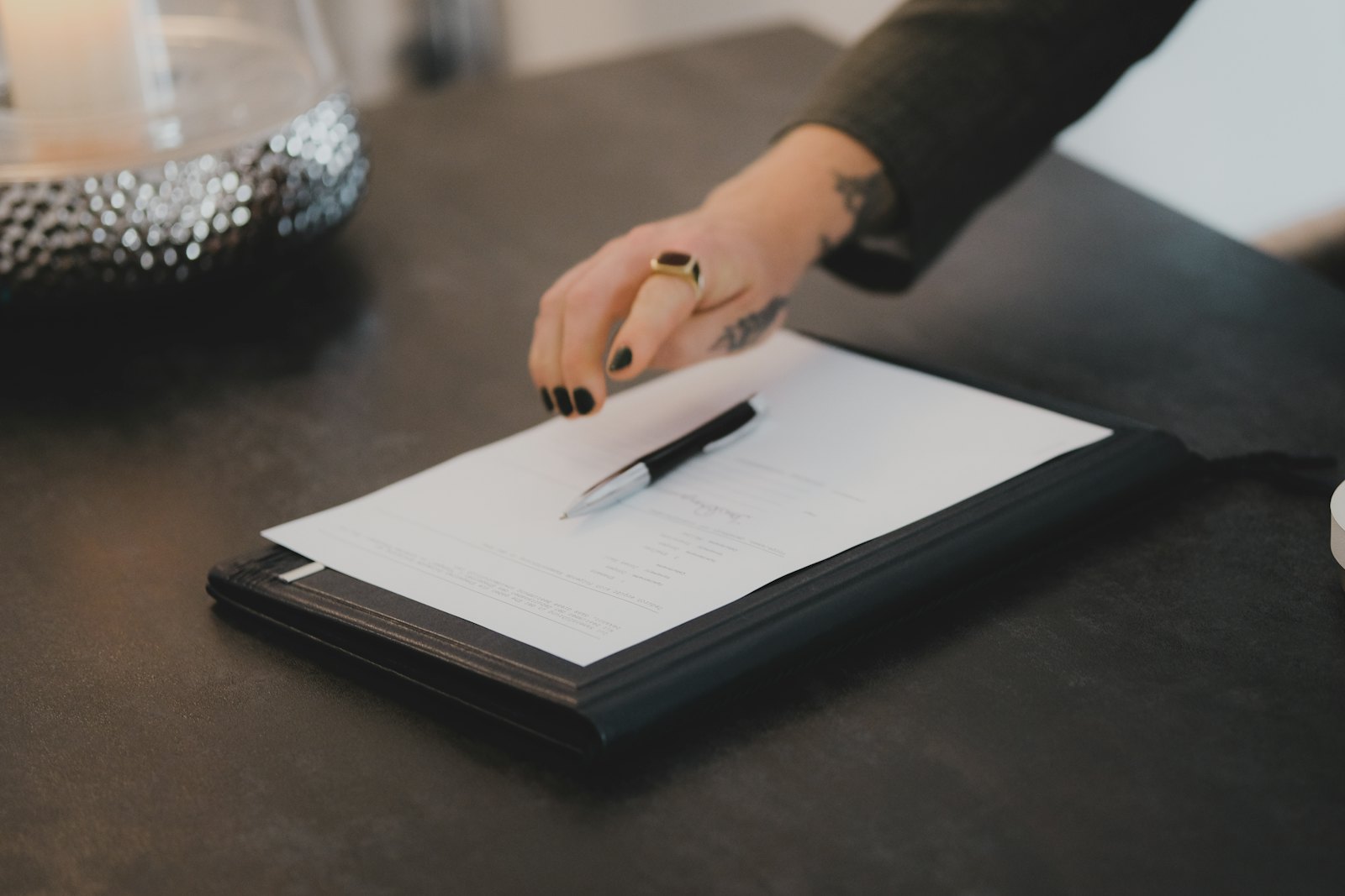 Main posant un stylo sur un document contractuel disposé dans un porte-documents, sur un bureau