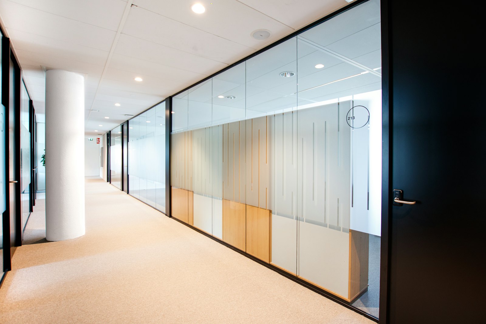 Couloir de bureaux à cloisons vitrées, éclairé en lumière du jour, desservant plusieurs salles de travail