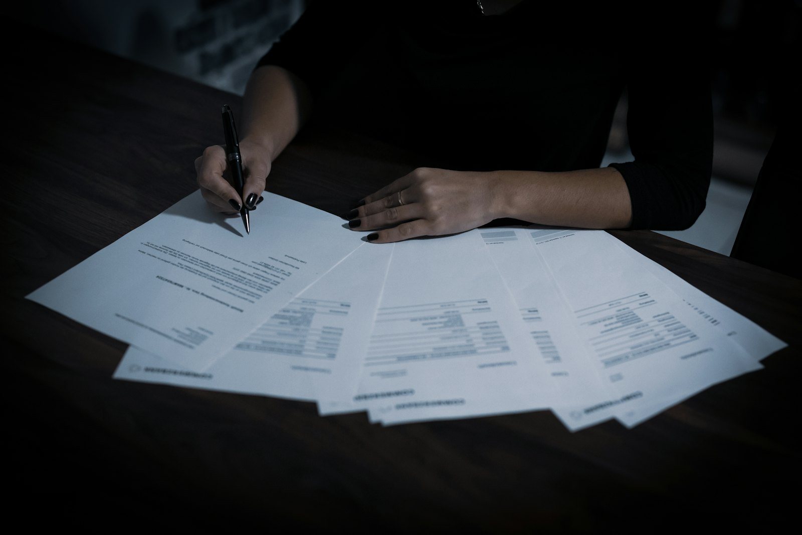 Personne assise à une table de bureau, stylo en main, qui parcourt les pages d'un contrat avant de le signer